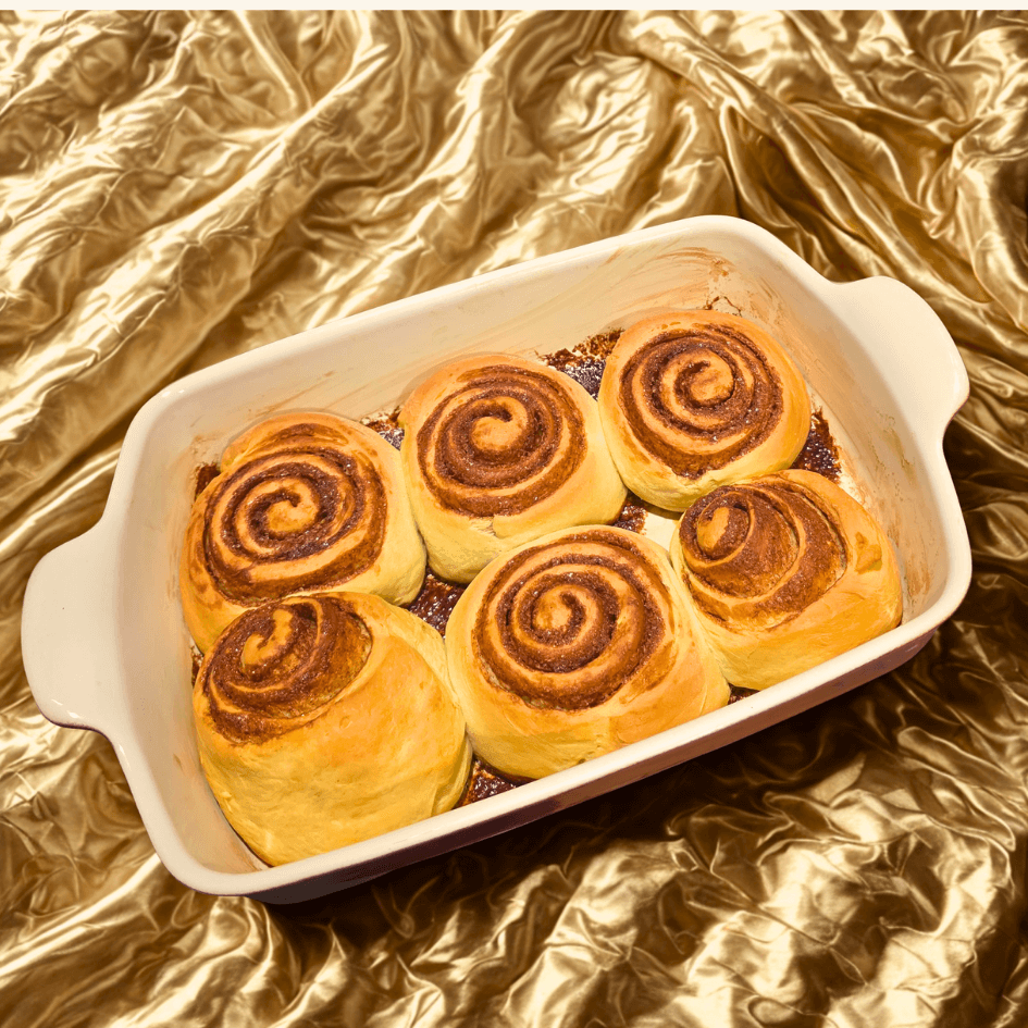 Freshly baked classic cinnamon rolls in a ceramic baking dish on a gold fabric backdrop.